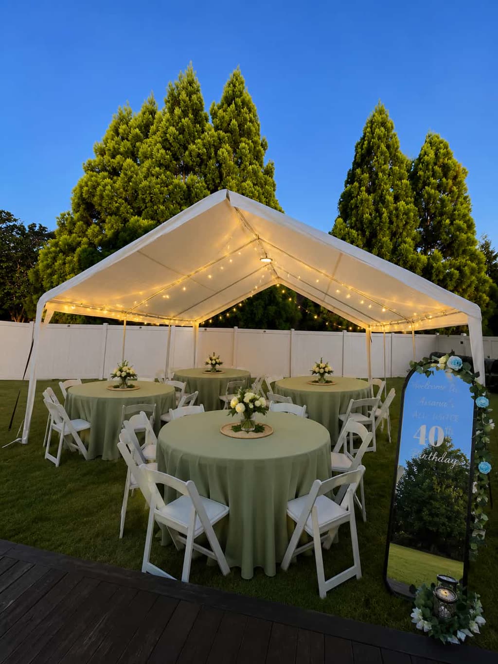 Sage green round tables under a lit white tent at dusk, finished setup