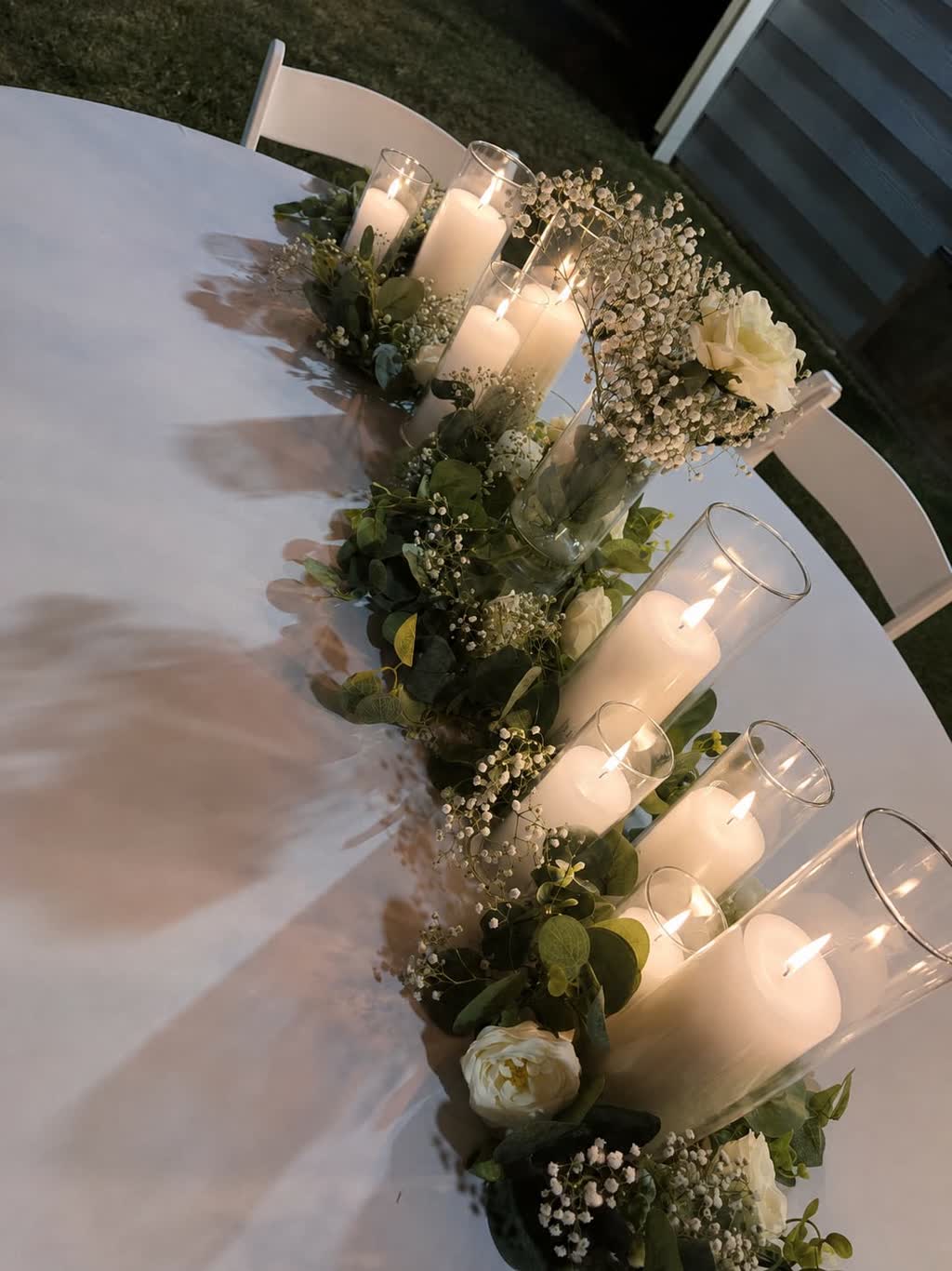 Candle centerpiece with eucalyptus, roses and baby's breath on a white banquet table