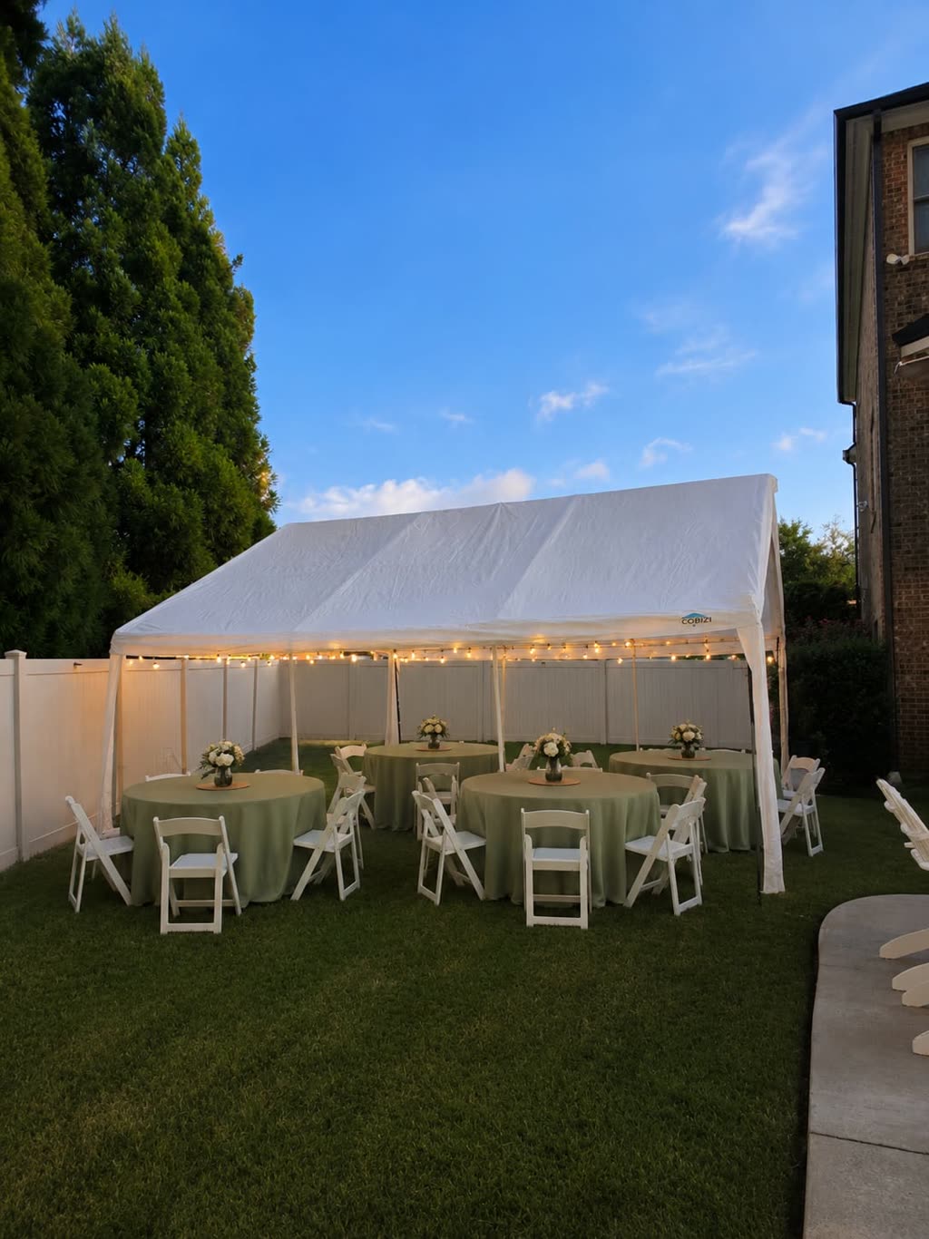 20x30 white tent at dusk with string lights and sage green round tables with white folding chairs