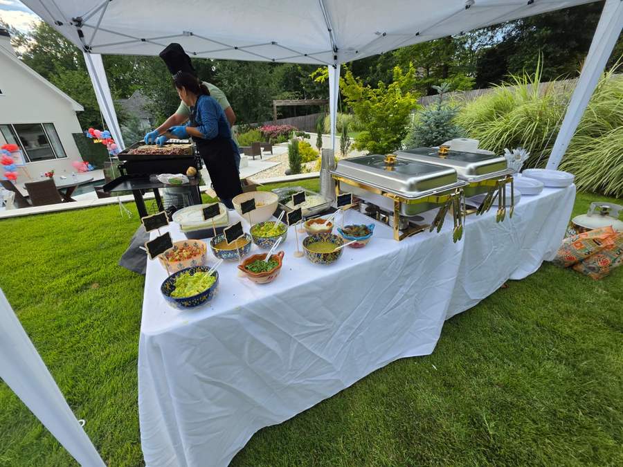 Cook grilling at a taquiza station under a canopy in a backyard