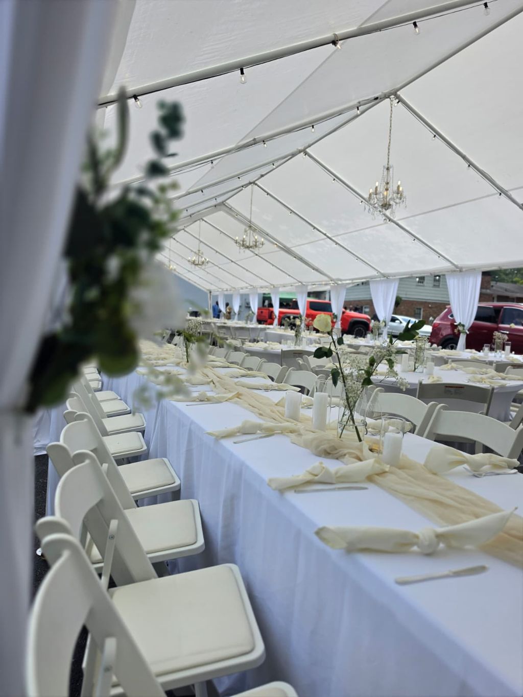 Draped tent ceiling with warm lights, pink bows and round tables on a lawn at night