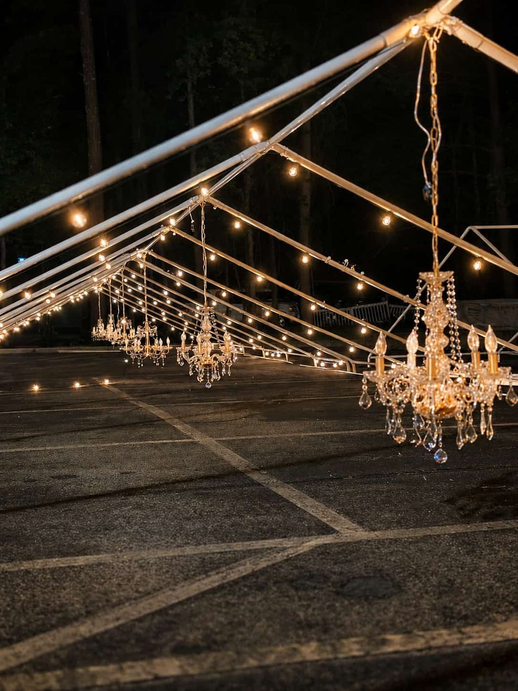 Long white frame tent with draped legs and warm perimeter lights on a paved lot at night