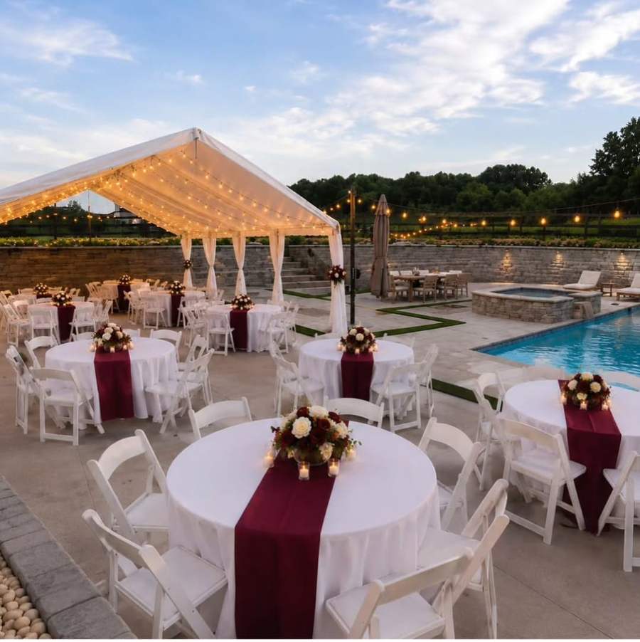 Round tables with burgundy runners beside a pool at sunset