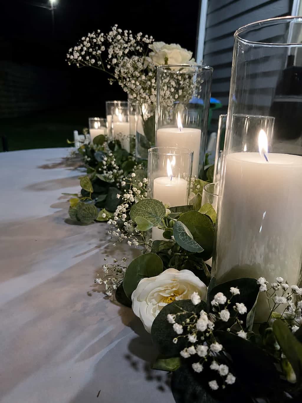 Glass hurricane candles and greenery garland along a head table at night