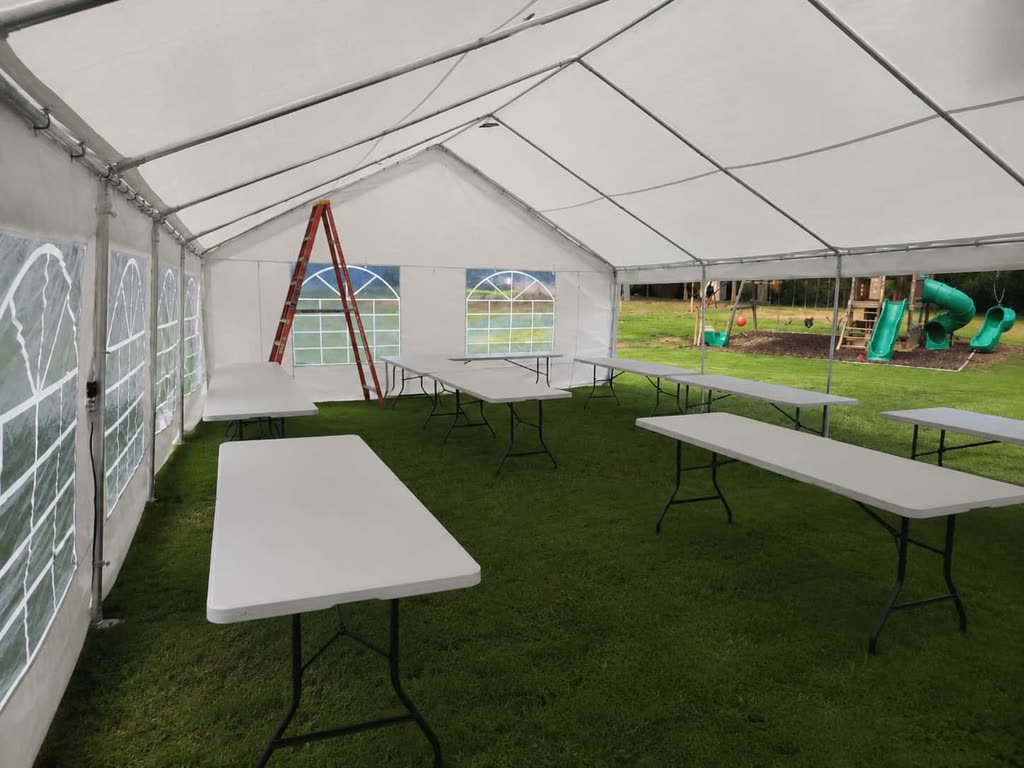 Interior of a 20x40 white tent with clear windows and rows of 8-foot folding tables on a green lawn