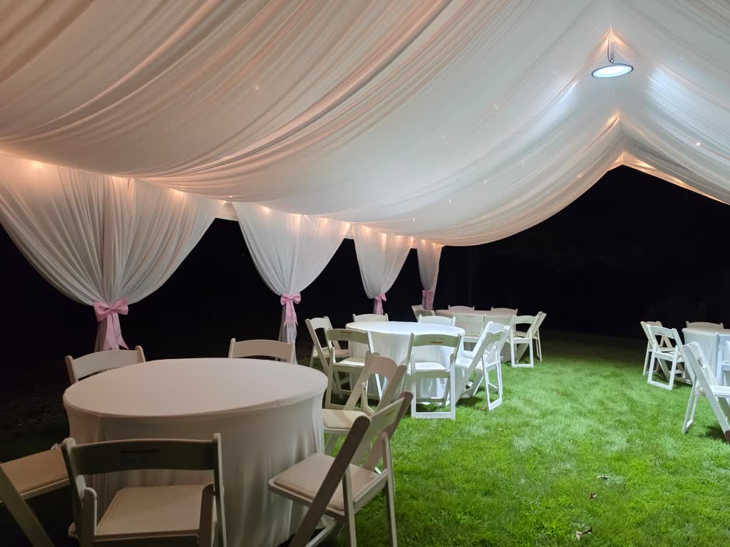 Draped tent interior lit at night with round tables and pink accents