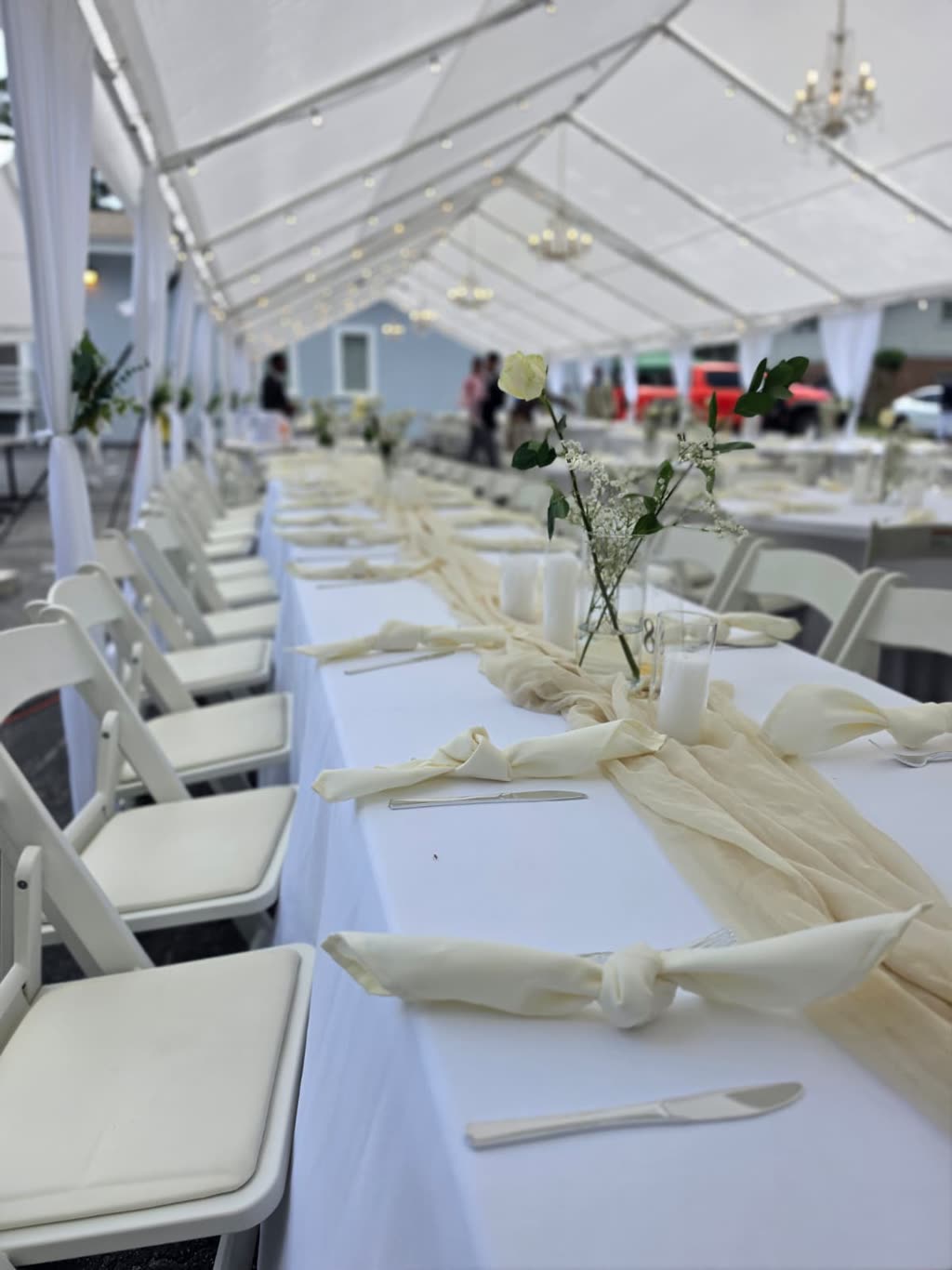 Long banquet table with ivory chiffon runner, knotted napkins and white rose bud vases under a tent — event setup in Avalon District, Alpharetta, GA