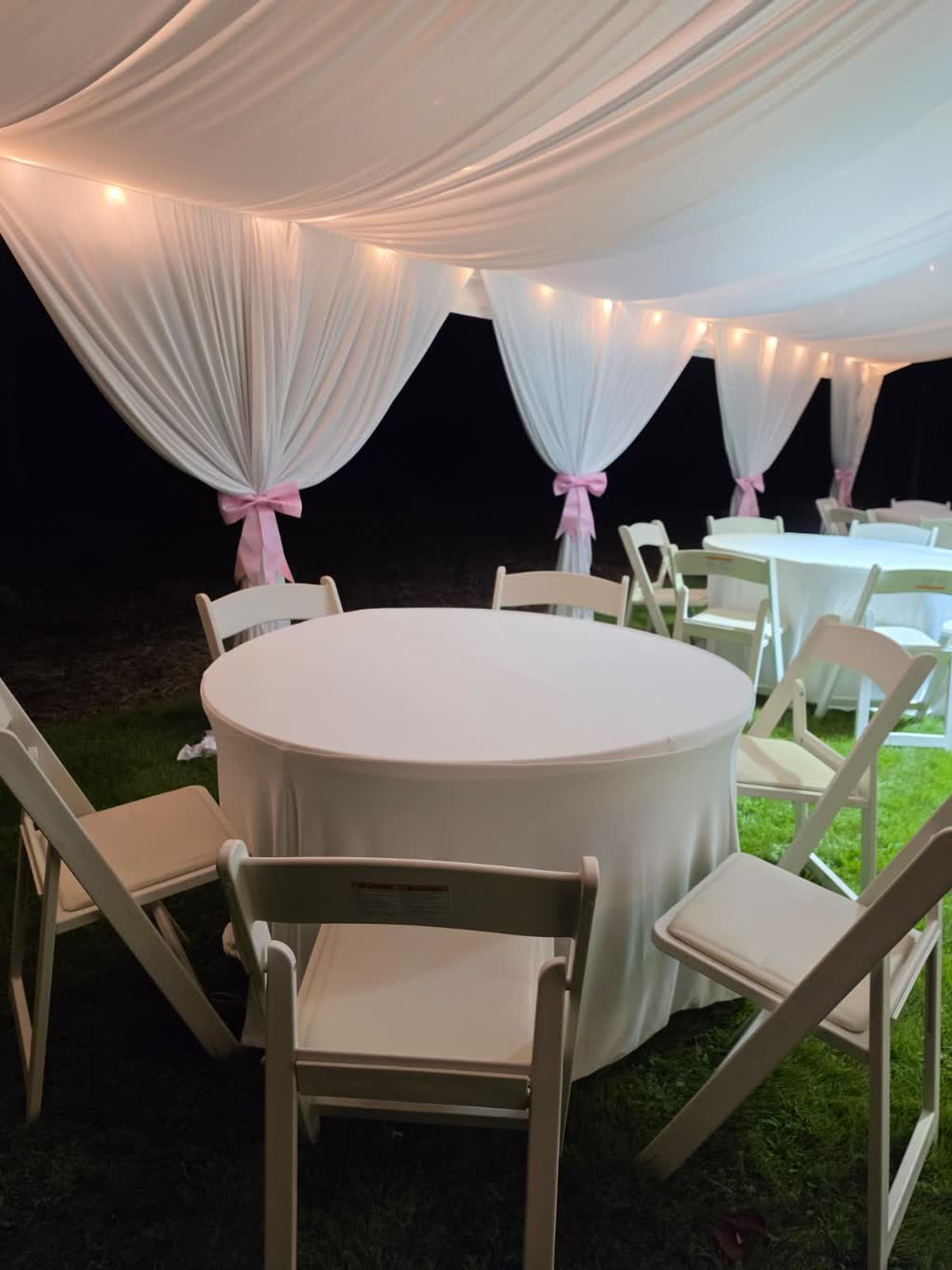 Round table with white linen and folding chairs under a draped tent at night